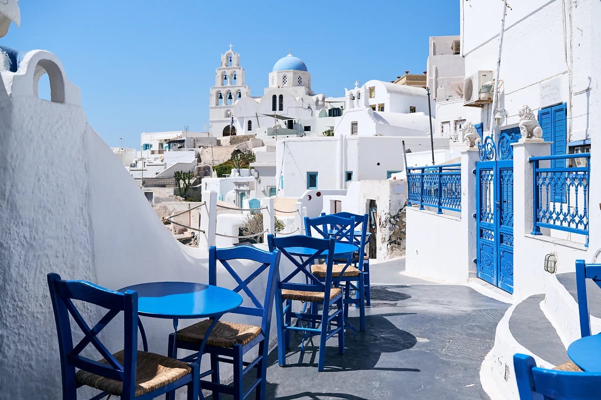 Rue typique avec des tables et des chaises bleues parmi les maisons blanches du village de Pyrgos, Santorin, Grèce